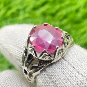 May include: A silver ring featuring a large, faceted, pink gemstone set in a crown-like design.