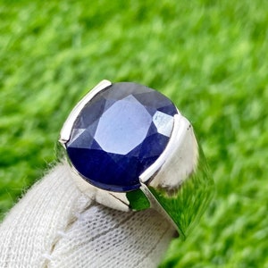 May include: A silver ring with a large, dark blue gemstone. The ring is set on a white cloth background.