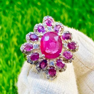 Puede incluir: Un anillo de plata con una gran piedra ovalada rosa rodeada de piedras más pequeñas de color rosa y blanco.