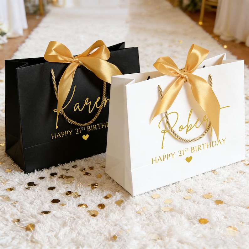 Peut inclure: Deux sacs cadeaux, un noir et un blanc, avec des n&oelig;uds et des poign&eacute;es dor&eacute;es. Le sac noir porte l'inscription "Karen" et "Happy 21st Birthday" en lettres dor&eacute;es. Le sac blanc porte l'inscription "Robert" et "Happy 21st Birthday".