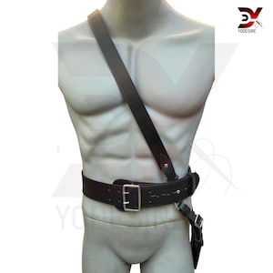 Pu&ograve; includere: Una cintura in pelle nera con fibbia argentata e una tracolla abbinata. La tracolla &egrave; indossata diagonalmente sul corpo.