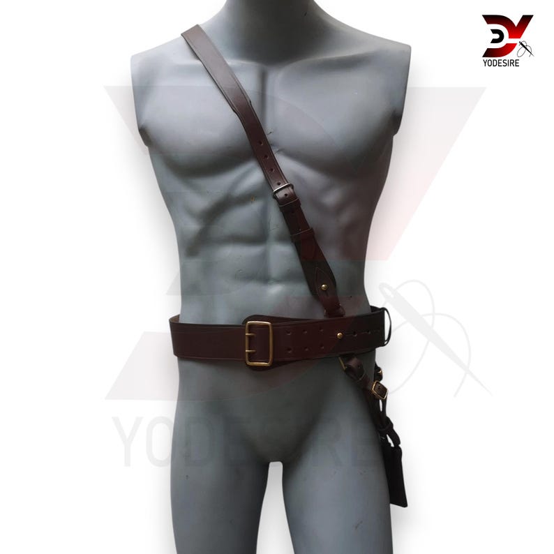 Pu&ograve; includere: Una cintura in pelle marrone con una fibbia dorata e una tracolla in pelle marrone abbinata. La tracolla &egrave; indossata sulla spalla e fissata alla cintura all'altezza del fianco.