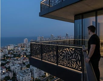 May include: A black metal balcony railing featuring a laser-cut organic leaf pattern with integrated LED lighting along the top edge. The railing is installed on a high-rise building overlooking a coastal city at dusk with a view of the ocean.