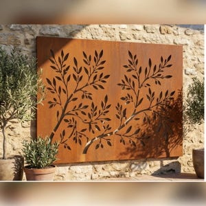 May include: A rectangular metal garden screen with a rusted finish featuring a laser-cut design of two olive tree branches with leaves and small olives. The panel is mounted against a light-coloured stone wall between two potted olive trees.
