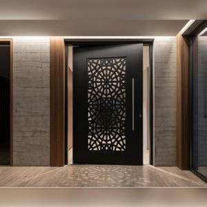 Peut inclure: Une porte d'entrée noire avec un motif géométrique découpé dans le panneau supérieur. La porte a une longue poignée argentée et est encastrée dans une entrée moderne avec des accents de béton et de bois. Le sol est en pierre claire.