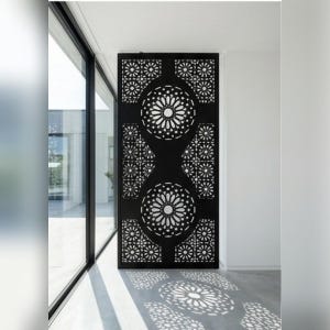 Peut inclure: Écran décoratif noir avec des motifs floraux et géométriques découpés. L'écran est placé devant une grande fenêtre, projetant des ombres décoratives sur le sol. Le design présente de grands motifs circulaires.