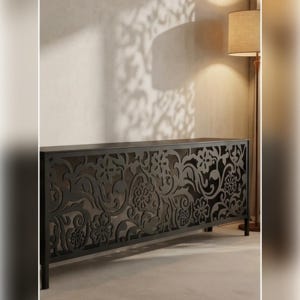 Peut inclure: Un cache-radiateur rectangulaire noir doté d'un motif floral et végétal complexe découpé au laser sur le panneau avant. La structure est soutenue par quatre pieds fins et se tient contre un mur, projetant des ombres détaillées au sol.