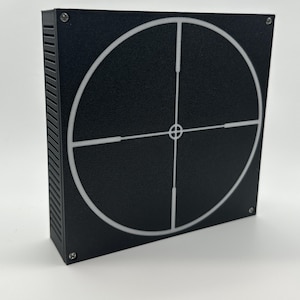 Könnte beinhalten: Ein schwarzes quadratisches Ziel mit einem weißen Kreis und einem Fadenkreuz in der Mitte. Das Ziel ist aus einem strukturierten Material gefertigt und hat einen leicht erhöhten Rand.