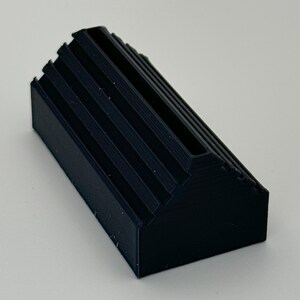 May include: A black plastic card holder with a ridged design. The holder has a slot for holding cards.