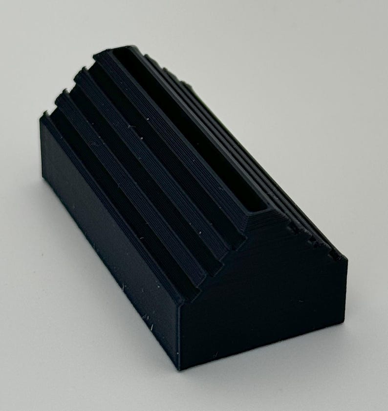 May include: A black plastic card holder with a ridged design. The holder has a slot for holding cards.