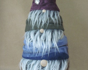 May include: A white-haired gnome with a purple hat, green scarf, and blue scarf. The gnome has a wooden nose and is standing on a brown surface.