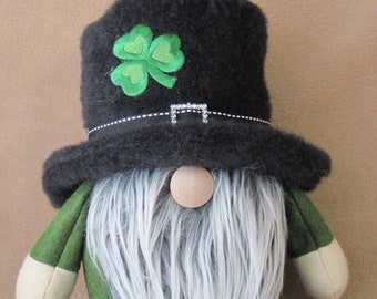 May include: A St. Patrick's Day gnome doll with a black hat adorned with a green shamrock and a silver buckle. The gnome has a long, white beard, a wooden nose, and green and black clothing. The doll is a festive decoration.