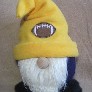 May include: A yellow gnome with a white beard and a black hat. The hat has a brown football design on the front.