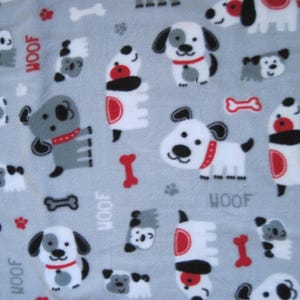 May include: Light blue fleece fabric with a repeating pattern of cartoon dogs in white, gray, and black, with red accents. The word "WOOF" is printed in red. The design includes dog bones and paw prints.