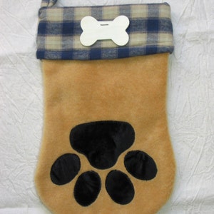 May include: A brown and tan Christmas stocking with a blue and white plaid cuff. The stocking has a paw print design and a white bone-shaped tag.