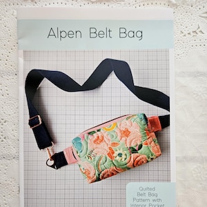 May include: A sewing pattern for a quilted belt bag with an interior pocket. The pattern is called "Alpen Belt Bag" and is by Center Street Quilts. The bag is shown in a floral fabric with a black strap.