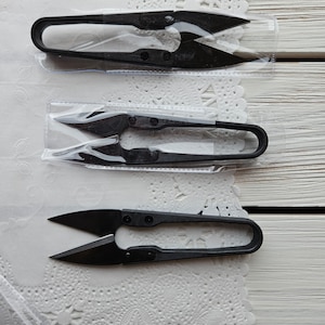 May include: Three black thread snips in individual plastic packaging. The snips are different sizes and have a sharp point.