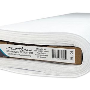 May include: A roll of white Moda Non-Woven Extra Firm interfacing fabric. The label indicates the fabric is 20 inches by 25 yards, machine washable, and dry cleanable. The roll is white and has a cardboard core.