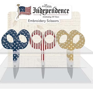May include: Three pairs of embroidery scissors with patriotic designs. One pair features a blue background with white stars, another has red and white stripes, and the third has a gold background with white stars. The display includes the text "Independence" and "Embroidery Scissors".