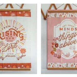 May include: Two decorative wall hangings with wooden rods. One is white with orange text that reads "From the rising of the sun" and floral accents. The other is pink with the text "Set your minds on things above" and floral designs.