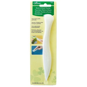 May include: A white Clover Point 2 Point Turner tool on a yellow and green package. The tool is curved with a pointed end and a rounded handle. Text on the package includes "Point 2 Point Turner" and instructions in multiple languages.