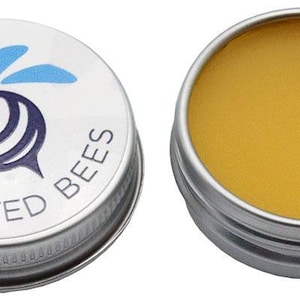 May include: Two small, round metal tins. One tin is open, revealing a yellow balm. The other tin has a silver lid with a cartoon bee graphic and the words "Twisted Bees". The bee is blue, black, and white.