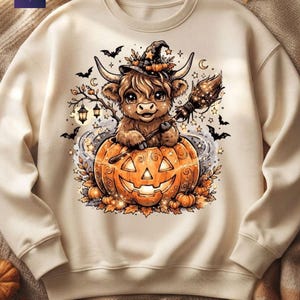 May include: A cream-colored crewneck sweatshirt featuring a graphic of a fluffy highland cow wearing a witch hat, holding a broomstick, and sitting inside a large carved jack-o'-lantern pumpkin surrounded by bats, stars, and lanterns.