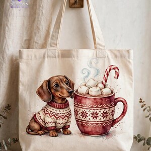 May include: A beige canvas tote bag featuring a watercolor illustration of a brown dachshund wearing a cream and red patterned sweater sitting next to a large red mug filled with marshmallows and a candy cane.
