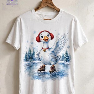 Puede incluir: Una camiseta blanca de manga corta con el gr&aacute;fico de un ganso blanco que lleva orejeras rojas, un collar rojo con un cascabel dorado y patines de hielo marrones sobre un estanque helado con pinos azules y copos de nieve.