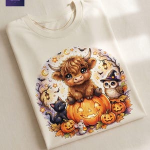 May include: A cream-colored t-shirt featuring a graphic of a fluffy highland cow sitting on a large jack-o'-lantern, accompanied by a black cat, a small mouse holding candy corn, and an owl wearing a witch hat, surrounded by stars and bats.