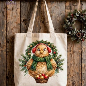 K&ouml;nnte beinhalten: Eine beigefarbene Stofftasche mit einer Grafik eines flauschigen braunen Vogels, der einen gr&uuml;nen Strickschal und rote Ohrensch&uuml;tzer tr&auml;gt. Der Vogel ist vor einem Tannenkranz abgebildet und h&auml;lt einen kleinen braunen Korb mit roten und goldenen Kugeln.