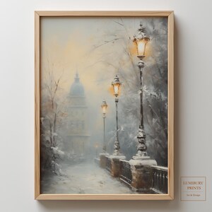 以下が含まれることがあります： 雪道と街灯が並ぶ冬景色を描いた額入りの絵画。背景には建物が描かれ、グレー、ブラウン、イエローの落ち着いた色使いが特徴です。「LUMIBURY PRINTS Art & Design」のサイン入り。