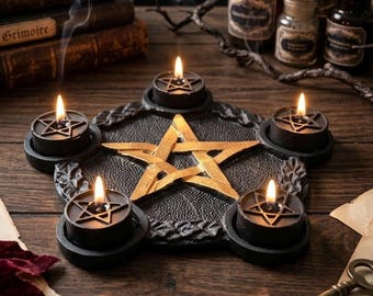 May include: A black pentagram-shaped candle holder featuring a central gold-colored star and five circular slots holding black tea light candles with lit flames. The base has a textured surface and is positioned on a dark wooden table.