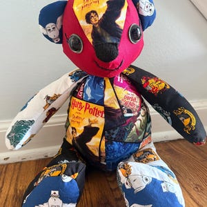 May include: A patchwork teddy bear constructed from various Harry Potter themed fabrics. The bear features a red face with black button eyes, and its body is covered in colorful prints depicting book covers, house crests, and white owls.