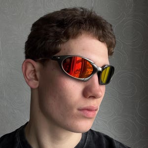 May include: Sport sunglasses with a dark gray frame and mirrored lenses. The lenses reflect a vibrant mix of red and yellow hues. The sunglasses have a sleek, curved design, suitable for outdoor activities.