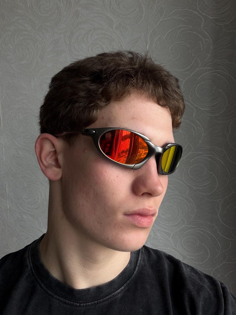 May include: Sport sunglasses with a dark gray frame and mirrored lenses. The lenses reflect a vibrant mix of red and yellow hues. The sunglasses have a sleek, curved design, suitable for outdoor activities.