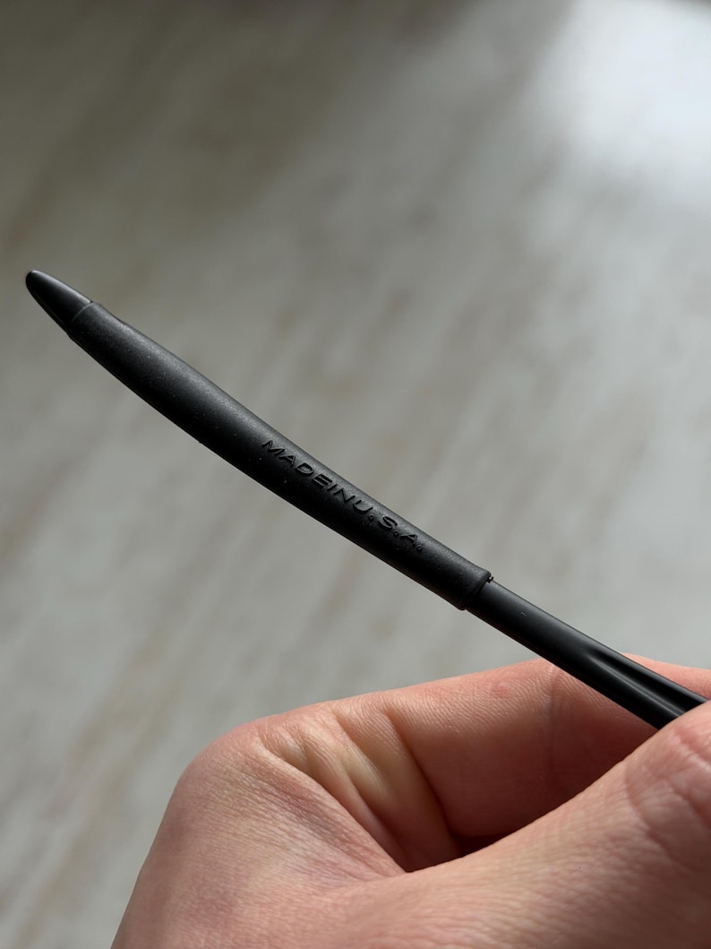 K&ouml;nnte beinhalten: Eine schwarze Stiftmine mit einer Spitze. Der Text "MADE IN U.S.A." ist auf dem Stift aufgedruckt. Der Stift wird von einer Person gehalten.