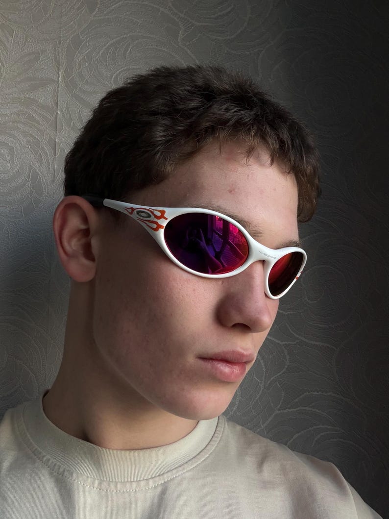 May include: White sunglasses with red mirrored lenses. The frames have a flame design in red and orange. The sunglasses are worn by a person.