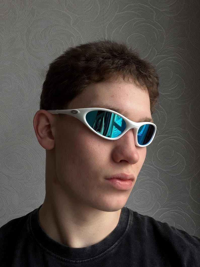 Puede incluir: Gafas de sol con montura blanca y lentes reflectantes azules. Las gafas deportivas presentan un dise&ntilde;o elegante y curvado. Las lentes reflejan un tono azul y las monturas son de color blanco brillante. Un accesorio moderno.