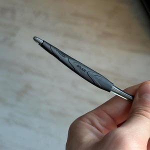 May include: A black and silver pen with the word "SPLICE" printed on the side. The pen has a textured grip and a silver tip. The pen is held in a hand.