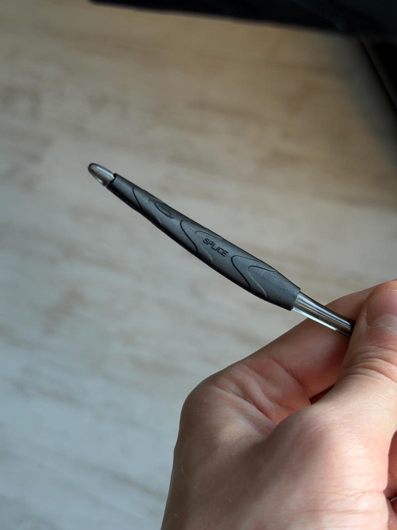 May include: A black and silver pen with the word "SPLICE" printed on the side. The pen has a textured grip and a silver tip. The pen is held in a hand.