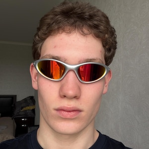 Puede incluir: Gafas de sol con montura plateada y lentes espejadas rojas y naranjas. Las gafas deportivas presentan un dise&ntilde;o elegante y envolvente. Las lentes reflejan un vibrante espectro de colores, ofreciendo una est&eacute;tica audaz y moderna. Protegen del sol.