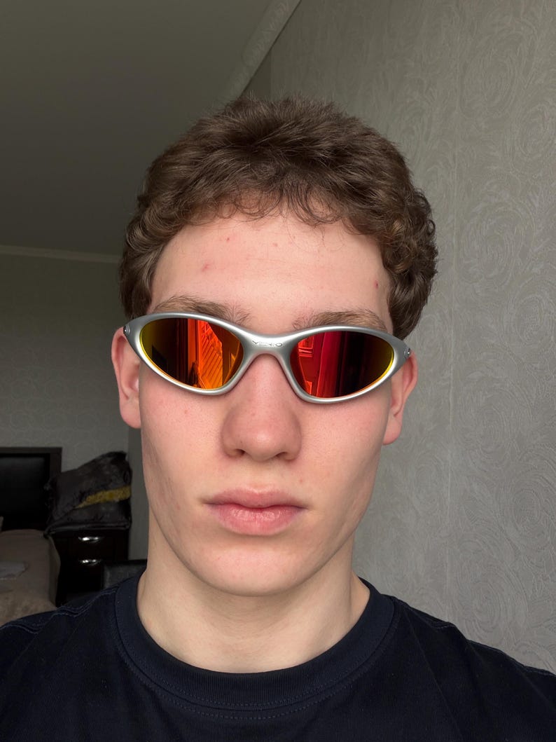 Puede incluir: Gafas de sol con montura plateada y lentes espejadas rojas y naranjas. Las gafas deportivas presentan un dise&ntilde;o elegante y envolvente. Las lentes reflejan un vibrante espectro de colores, ofreciendo una est&eacute;tica audaz y moderna. Protegen del sol.