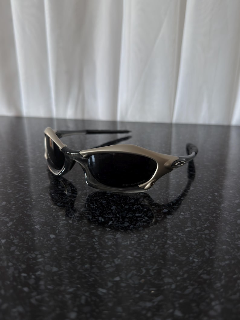 May include: Sport sunglasses with a silver frame and dark lenses. The sunglasses have a sleek, modern design with a curved shape. The lenses are dark, providing protection from the sun. The frame is a metallic silver color.