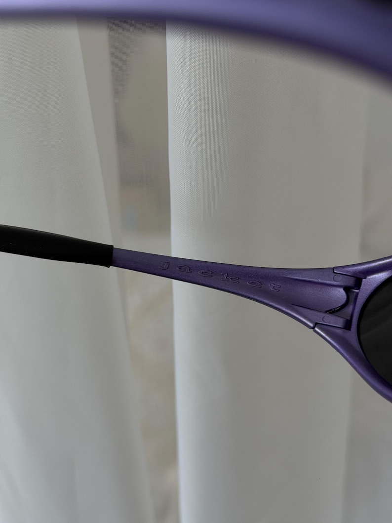 May include: Close-up of purple sunglasses with black arms. The text "jaguar" is printed on the arm of the sunglasses. The sunglasses have dark lenses and a sleek, modern design.