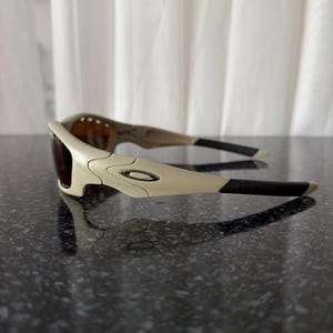 May include: Off-white sunglasses with dark lenses and black temples. The sunglasses have a curved design with a small silver logo on the frame. The lenses are a dark brown color.