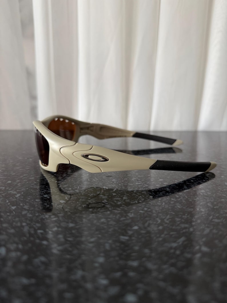 May include: Off-white sunglasses with dark lenses and black temples. The sunglasses have a curved design with a small silver logo on the frame. The lenses are a dark brown color.