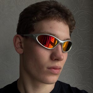 Puede incluir: Gafas de sol con montura plateada y lente espejada roja y naranja vibrante. El dise&ntilde;o elegante y deportivo presenta una montura curvada y una est&eacute;tica aerodin&aacute;mica. Las lentes reflejan el entorno.