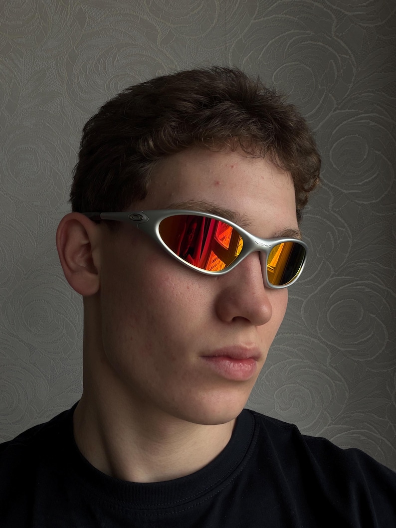 Puede incluir: Gafas de sol con montura plateada y lente espejada roja y naranja vibrante. El dise&ntilde;o elegante y deportivo presenta una montura curvada y una est&eacute;tica aerodin&aacute;mica. Las lentes reflejan el entorno.