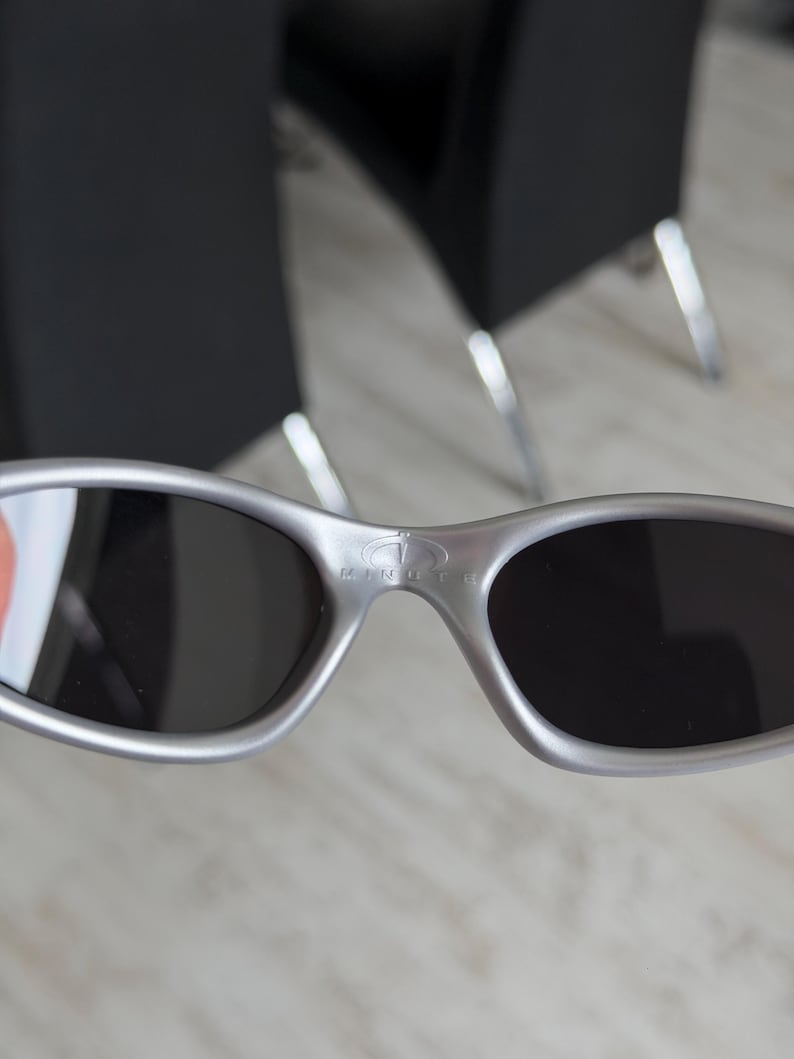 May include: Silver-framed sunglasses with dark lenses. The sunglasses have an oval shape and a bridge with the brand name "KINGTH" printed on it. The sunglasses are a metallic silver color.